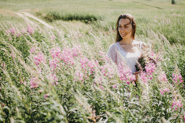 A young woman in a dress walks in a field of blooming willow-tea