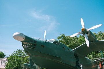 nose of the old military aircraft of green. Old military aircraft in green with white propellers against a blue sky. monument of military aircraft on the background of trees and sky