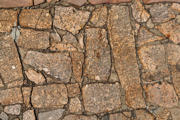 The texture of the sidewalk of chaotic granite stones of different colors with many cracks