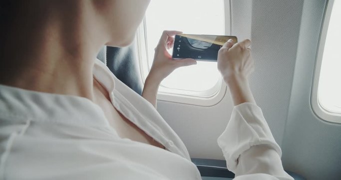 Asian woman using smartphone taking a picture through the airplane windows while her travel to do a business