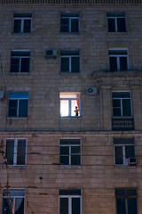 silhouette of a child in the illuminated window of an apartment building in the evening