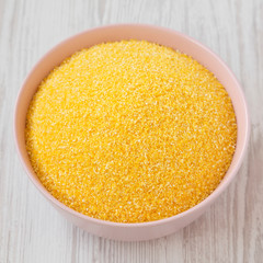 Dry organic Masarepa corn meal in a pink bowl over white wooden surface, low angle view. Close-up.