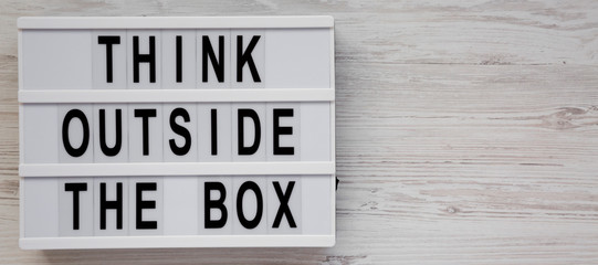 Lightbox with 'Think outside the box' words on a white wooden background, top view. Flat lay, overhead, from above. Copy space.