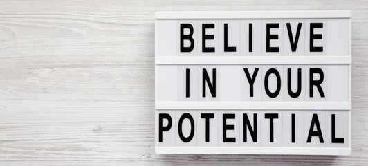 'Believe in your potential' words on a lightbox on a white wooden surface, top view. Space for text.