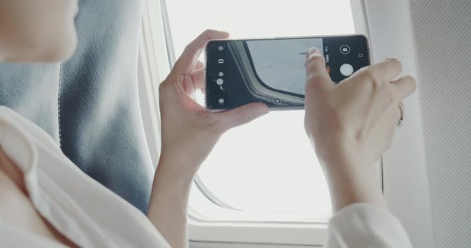 Asian woman using smartphone taking a picture through the airplane windows while her travel to do a business