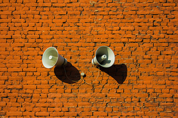 White loudspeakers attached to a red brick wall, background