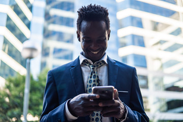 African American businessman holding mobile phone wearing blue suit and using modern smartphone near office. Business concept