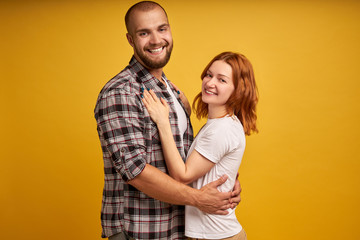 Fototapeta premium Photo of cheerful lovely family coupe cuddle each other, have fun together, look with big love and affection, wear stylish clothes, isolated over yellow background. People and closeness concept