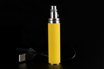Yellow battery and charger from an electronic cigarette on a black background in the studio