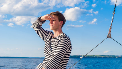 young male yachtsman looks into the distance - obrazy, fototapety, plakaty