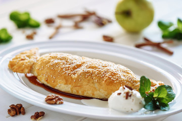 Apple Pastry Strudel Cake Sweet Dessert Closeup. Traditional Austrian Puff Pie with Vanila and Mint Leaf on White Plate. Bakery Food with Walnut and Fruit. Homemade Apfelstrudel Gourmet Ice Cream