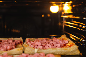 Homemade pizza in the oven close-up, sausage sprinkled with cheese