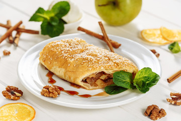 Apple Pastry Strudel Cake Tasty Dessert Closeup. Austrian Puff Piece with Cinnamon and Sesame, Mint Leaf on White Plate. Homemade Apfelstrudel Cutted for Delicious Sweet Healthy Fruit Breakfast.