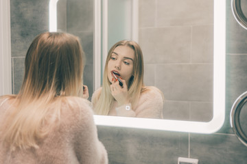 The girl in the bathroom in front of the mirror paints her lips.