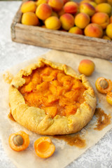 Homemade fruit pie (galette) made with fresh organic apricotes, top view. Open pie, apricot tart. Fruit bakery. Summer food, summer pie on parchment paper. Wooden box with apricots.