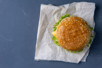 Burger with beef patty, salad, a slice of tomato and cheese, onions and sauce with paprika in a grilled bun with sesame