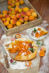 Homemade fruit pie (galette) made with fresh organic apricotes with powdered sugar on wooden table, top view. Plate with a cut piece of cake. Open pie, apricot tart on parchment paper.