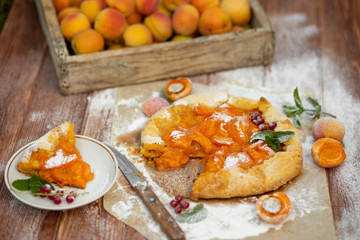 Fototapeta na wymiar Homemade fruit pie (galette) made with fresh organic apricotes with powdered sugar on wooden table, top view. Plate with a cut piece of cake. Open pie, apricot tart on parchment paper.