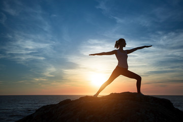 Woman yoga silhouette, performs concentration exercises during sunset on the sea coast.