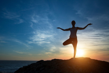 Woman yoga silhouette, performs concentration exercises during sunset on the sea coast.