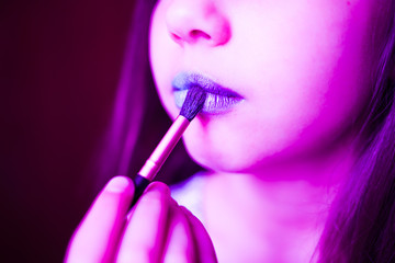 Girl in neon light with blue lipsteak on her lips.