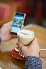 man with coffee and smartphone in hands, close-up large latte