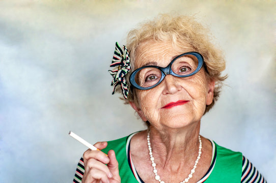 Old wrinkled fashionable woman in glasses with a cigarette in ha