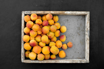 Wooden box with apricots on black background, top view.