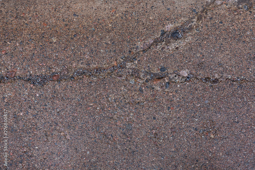 Poster close-up of a wet, weathered and cracked concrete footpath surface with pebbles (also known as pebbl