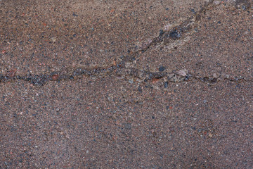 Close-up of a wet, weathered and cracked concrete footpath surface with pebbles (also known as pebblecrete or exposed aggregate), viewed from above. High resolution full frame textured background.