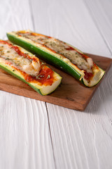 Two fresh hot zucchini boats with red sauce and melted cheese on cutting board.