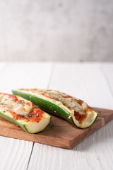 Two fresh hot zucchini boats with red sauce and melted cheese on cutting board.
