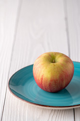 Red green apple on a green blue plate an white farmhouse table.