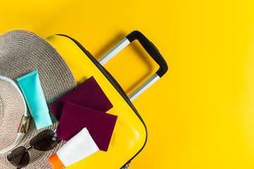 Bright and stylish cabin size suitcase with straw hat, sunscreen and passports flat lay. Easy travel with little baggage concept. Copy space.