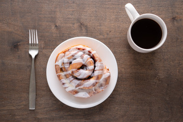 Large gourmet frosted cinnamon roll on brown distressed table.
