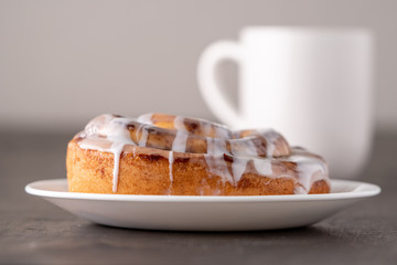 Large gourmet frosted cinnamon roll on brown distressed table.