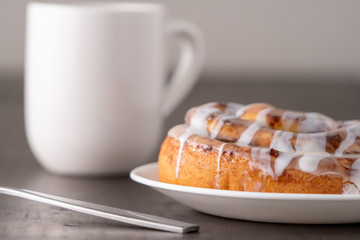 Large gourmet frosted cinnamon roll on brown distressed table.