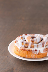 Large gourmet frosted cinnamon roll on brown distressed table.