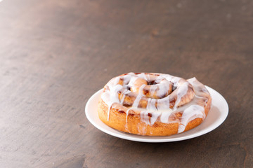 Large gourmet frosted cinnamon roll on brown distressed table.