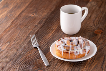 Large gourmet frosted cinnamon roll on brown distressed table.