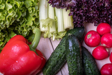 fresh vegetables on a light wooden table, paprika, celery, leaves of lettuce, cucumbers and radishes