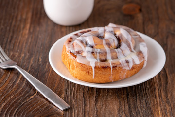 Large gourmet frosted cinnamon roll on brown distressed table.