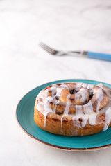 Large gourmet frosted cinnamon roll on marble table.