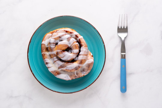 Large gourmet frosted cinnamon roll on marble table.