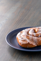 Large fresh frosted cinnamon roll on blue plate and table.