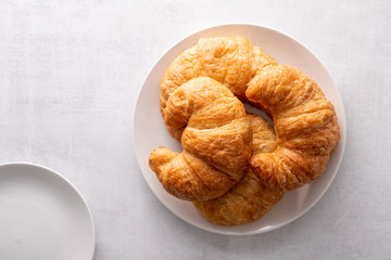 Warm crispy flaky croissant roll on white plate and distressed table.