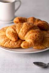 Warm crispy flaky croissant roll on white plate and distressed table.