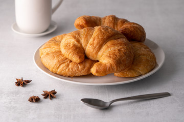 Warm crispy flaky croissant roll on white plate and distressed table.