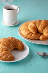Warm crispy flaky croissant roll on white plate and distressed table.