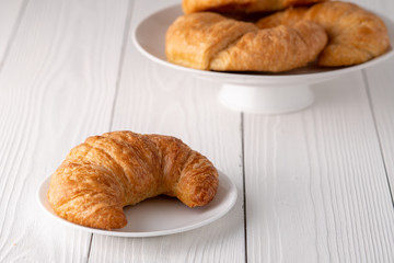 Warm crispy flaky croissant roll on white plate and distressed table.